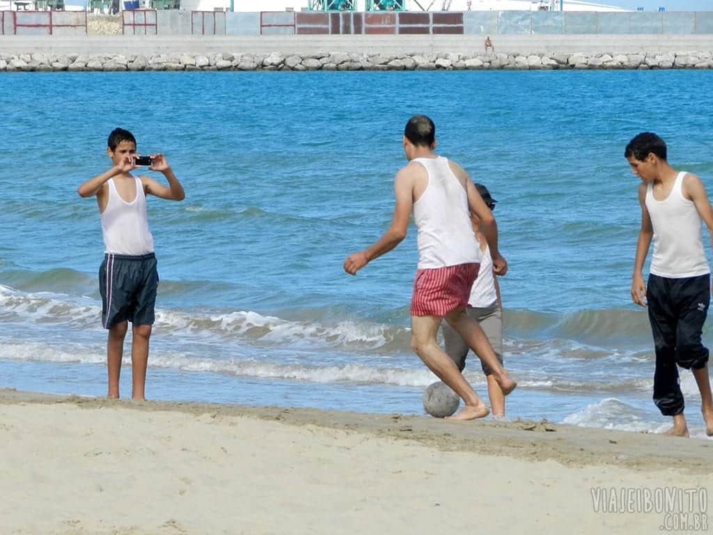 Imagem de crianças jogando bola na beira da praia.