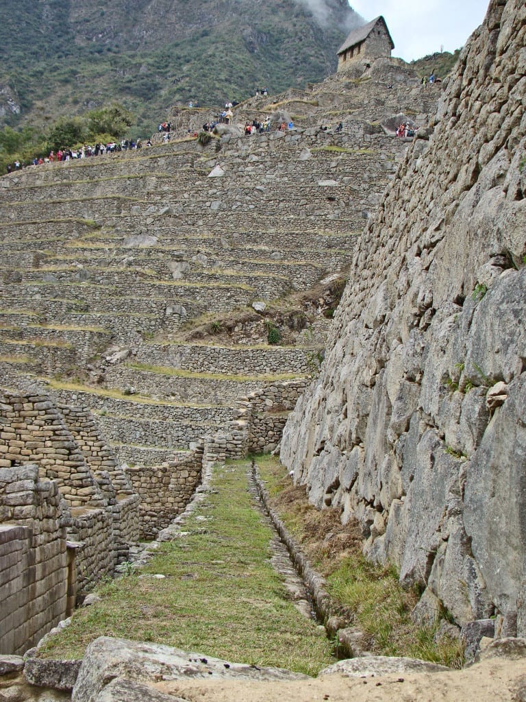 Terrazas agrícolas que utilizadas para cultivar alimentos e para dar suporte à cidadela de Machu Picchu, evitando a erosão do solo. Do lado direito, corre água em um dos muitos canais que levam até as fontes do lugar