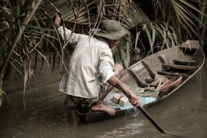 Homem de cócoras na ponta da canoa no Delta do Rio Mekong, próximo a Ho Chi Minh, Vietnã