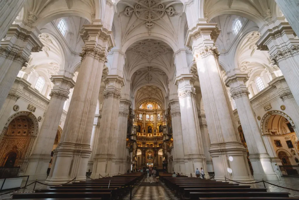 Interior da Catedral de Granada com grandes pilares brancos e altares dourados.